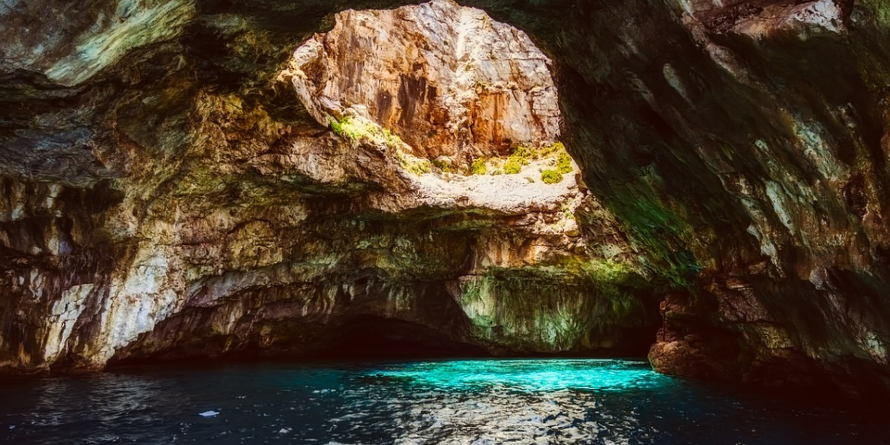 Foto di una grotta marina, la luce dall'alto illumina l'acqua e la colora di verde e azzurro